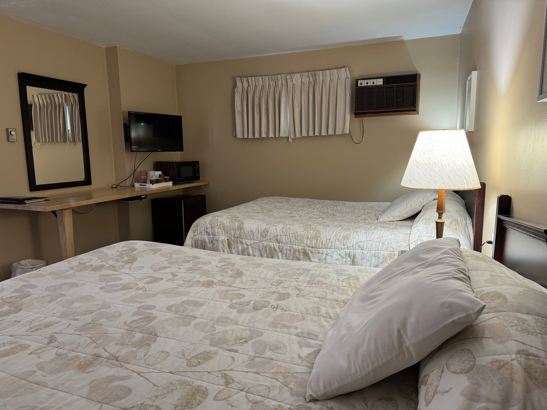 A hotel room with two beds , a lamp , a mirror and a television.