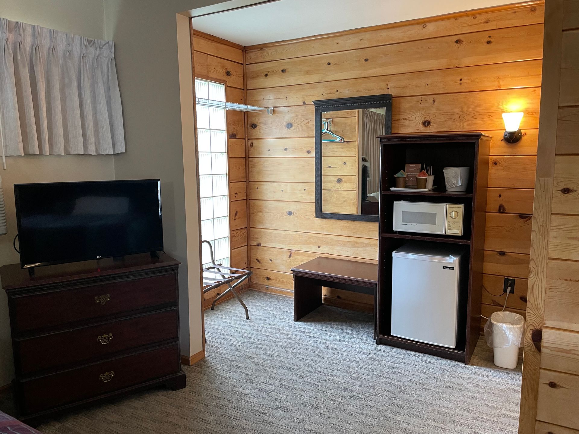 A hotel room with a flat screen tv , dresser , microwave and refrigerator.