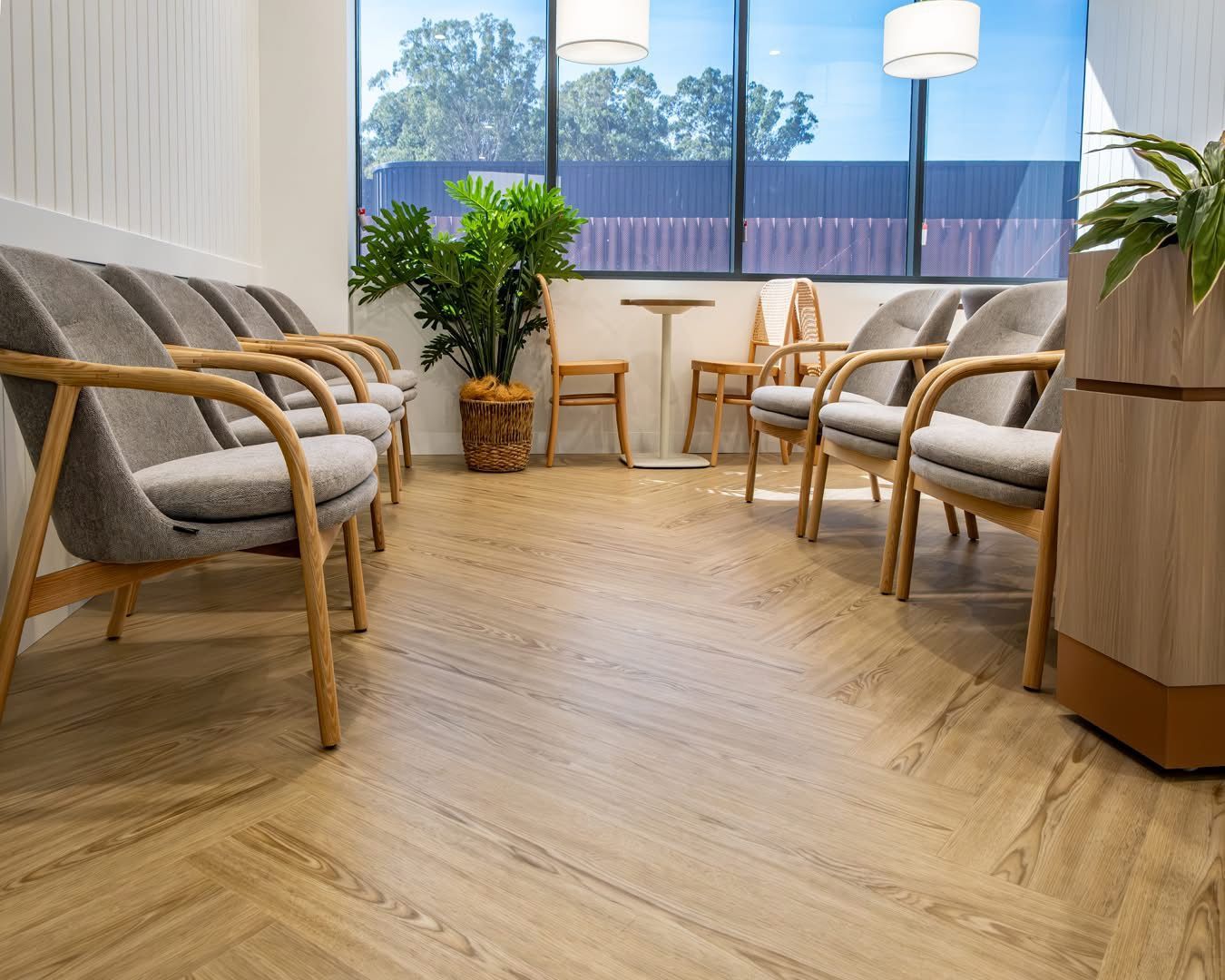 Waiting room with gray chairs, wood accents, and plants. Bright, modern space with a large window — Kelwin Coastal Carpets In Kundra Park, QLD