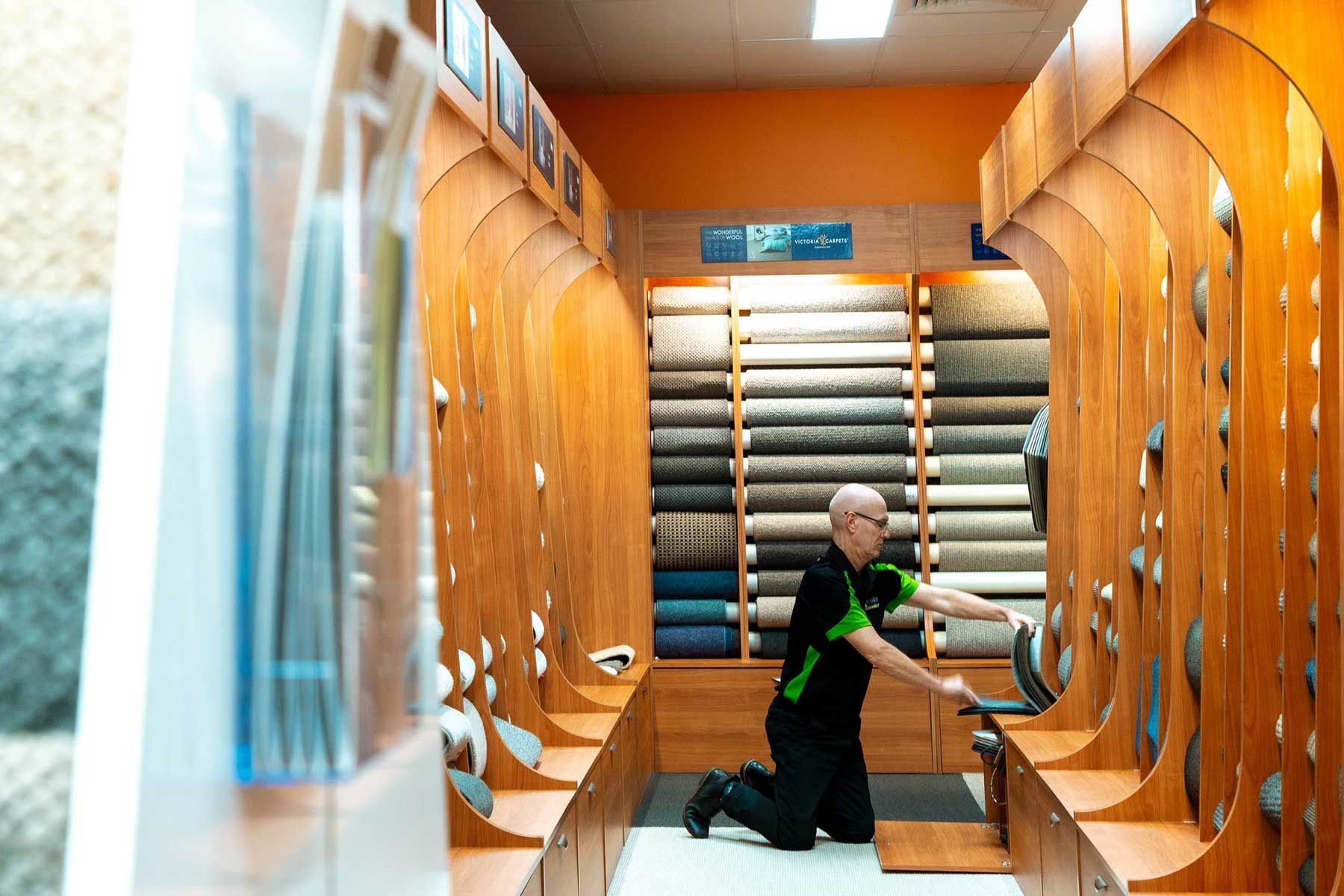 A Man Is Kneeling Down in A Carpet Store — Kelwin Coastal Carpets In Kundra Park, QLD