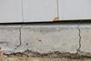 Cracked concrete foundation beneath white siding with a visible gap and crumbling edge