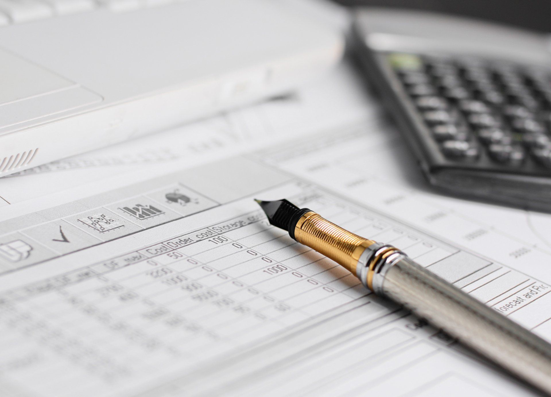 Calcolatrice e penna su documenti finanziari accanto a un computer portatile.