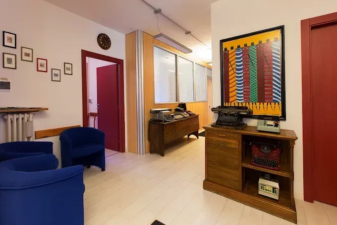 Luminoso soggiorno con sedie blu, mobili in legno, opere d'arte alle pareti e una porta che conduce a un corridoio.