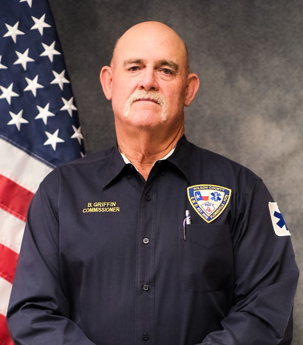 A man wearing a cowboy hat and a blue shirt is standing in front of a wall.