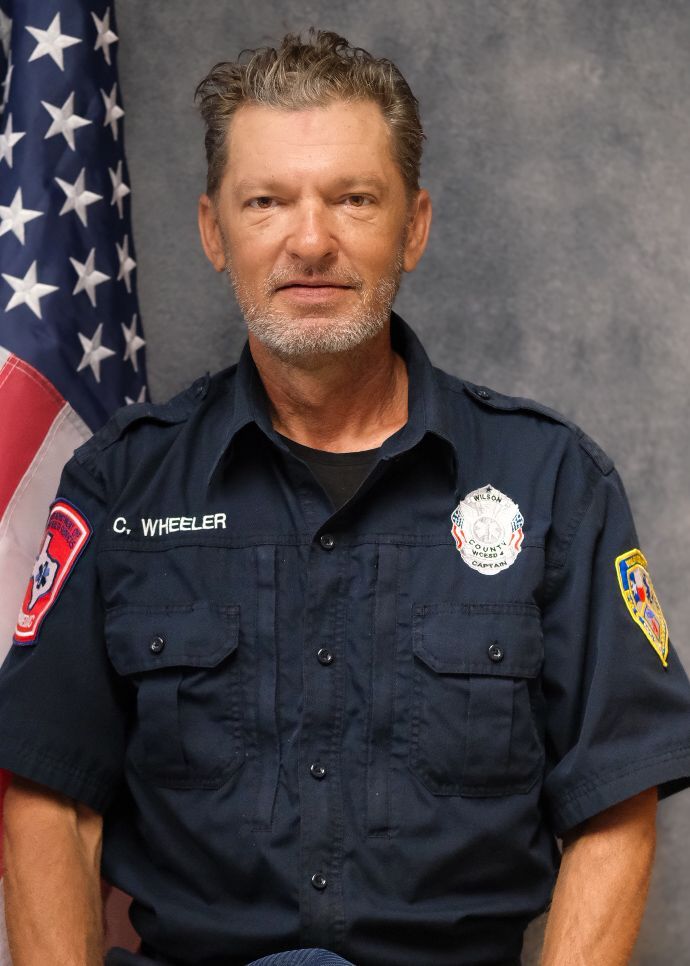 A man wearing a hat and a jacket is standing in front of a white wall.