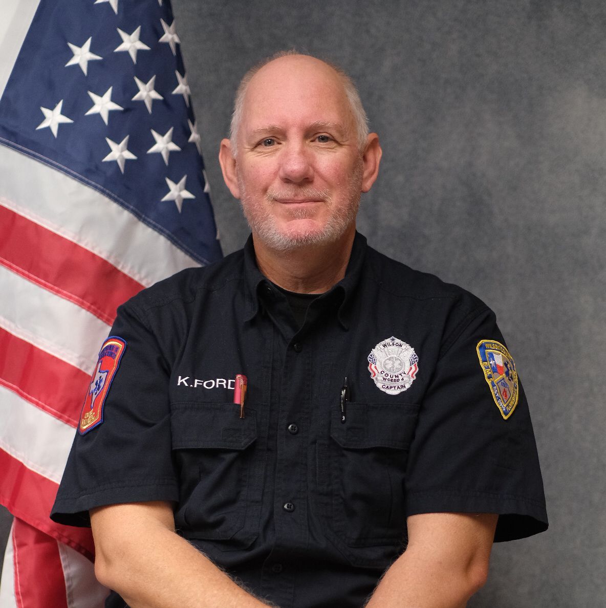 A man wearing a hat and sunglasses is standing in front of a white wall.