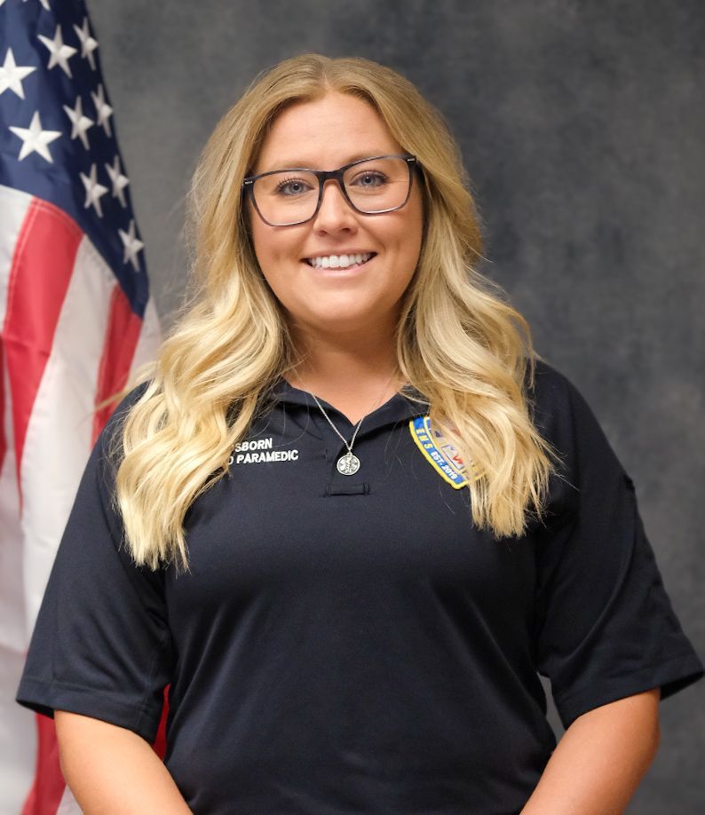 A man wearing a black shirt with a patch on it is smiling for the camera.