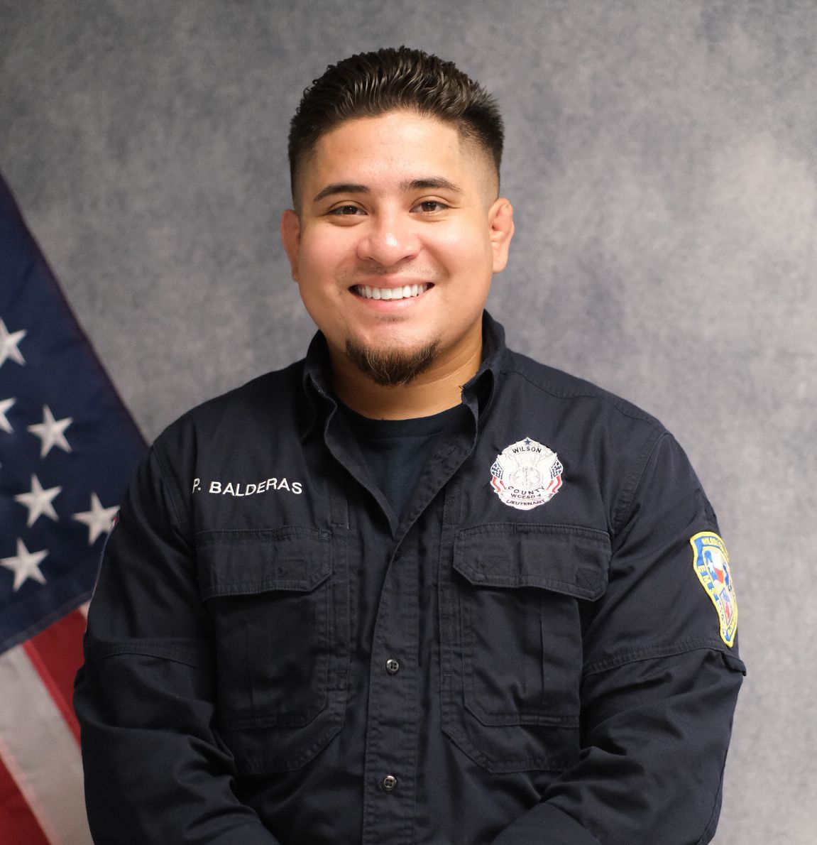 A man wearing a hat and sunglasses is standing in front of a white wall.