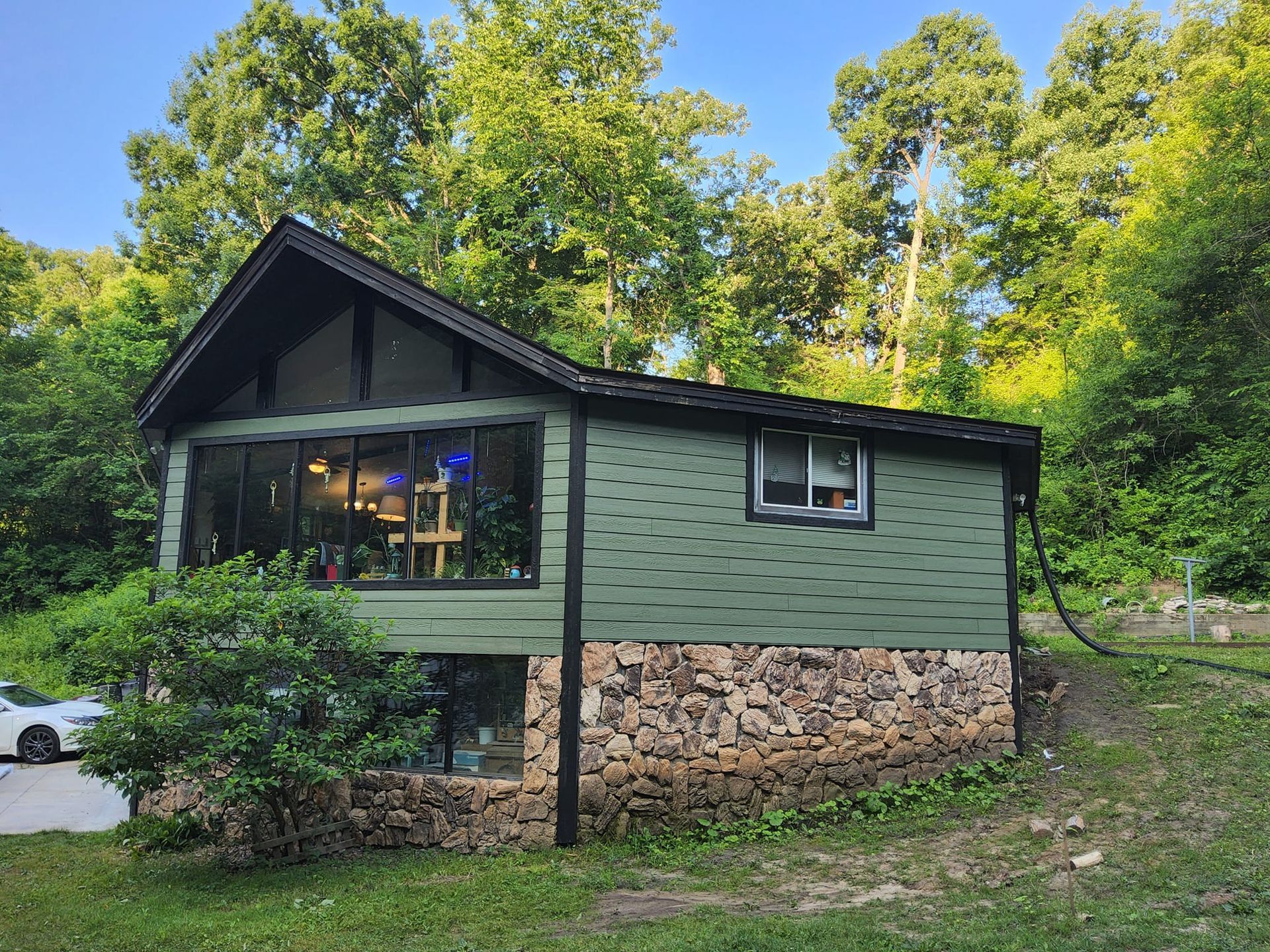 A small green house with a stone base is surrounded by trees.