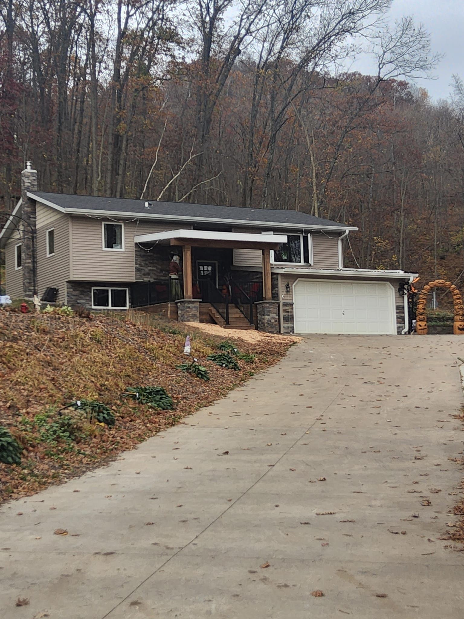 A house with a garage is sitting on top of a hill in the woods.