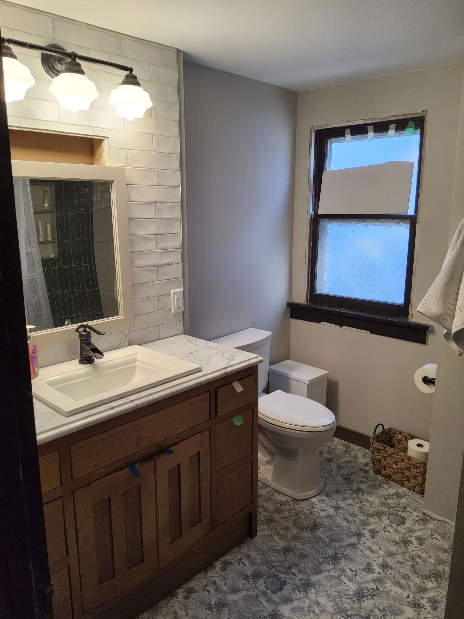 A bathroom with a sink , toilet , mirror and window.