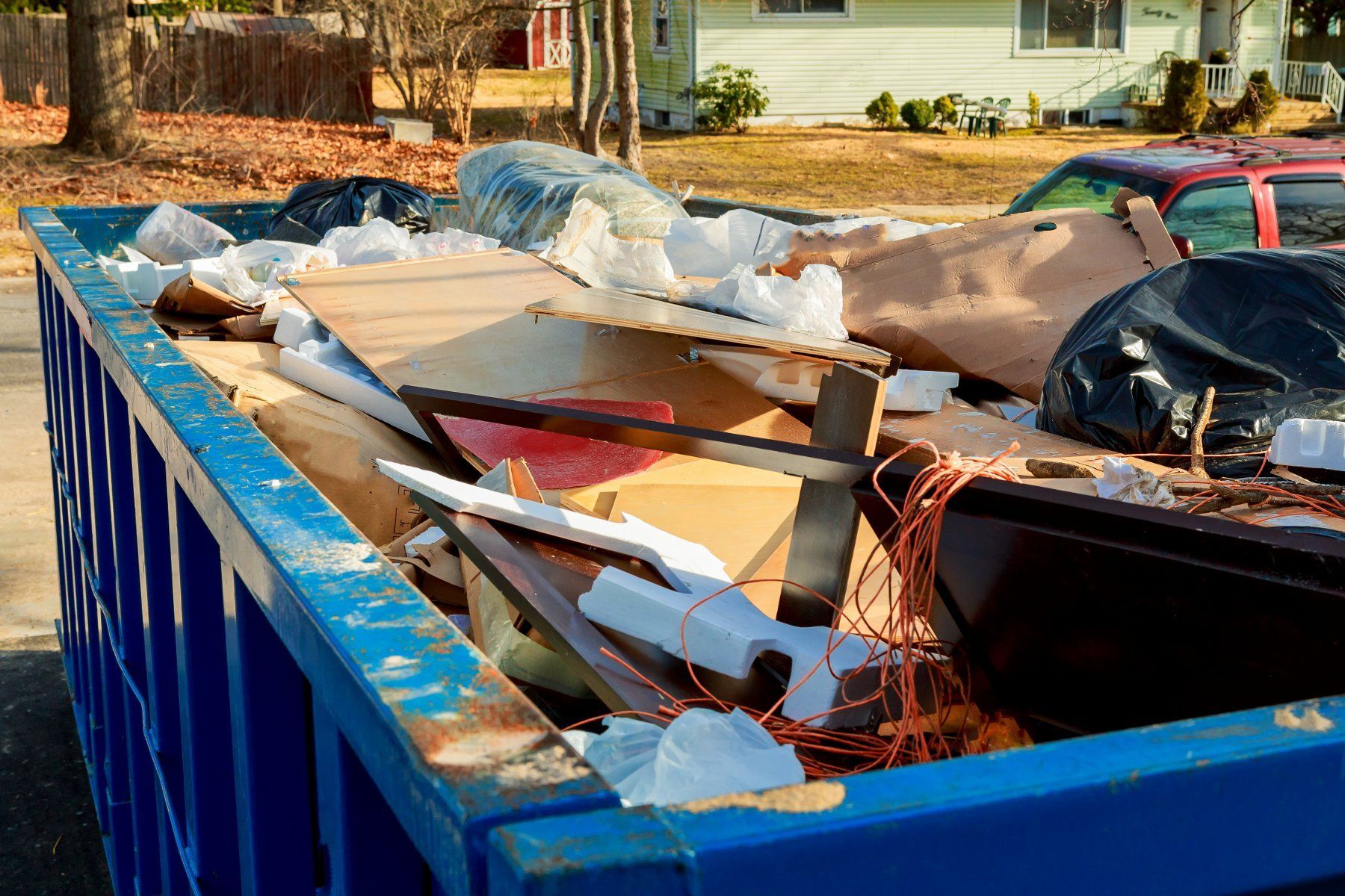 Blue dumpster filled with construction debris, cardboard, and trash.