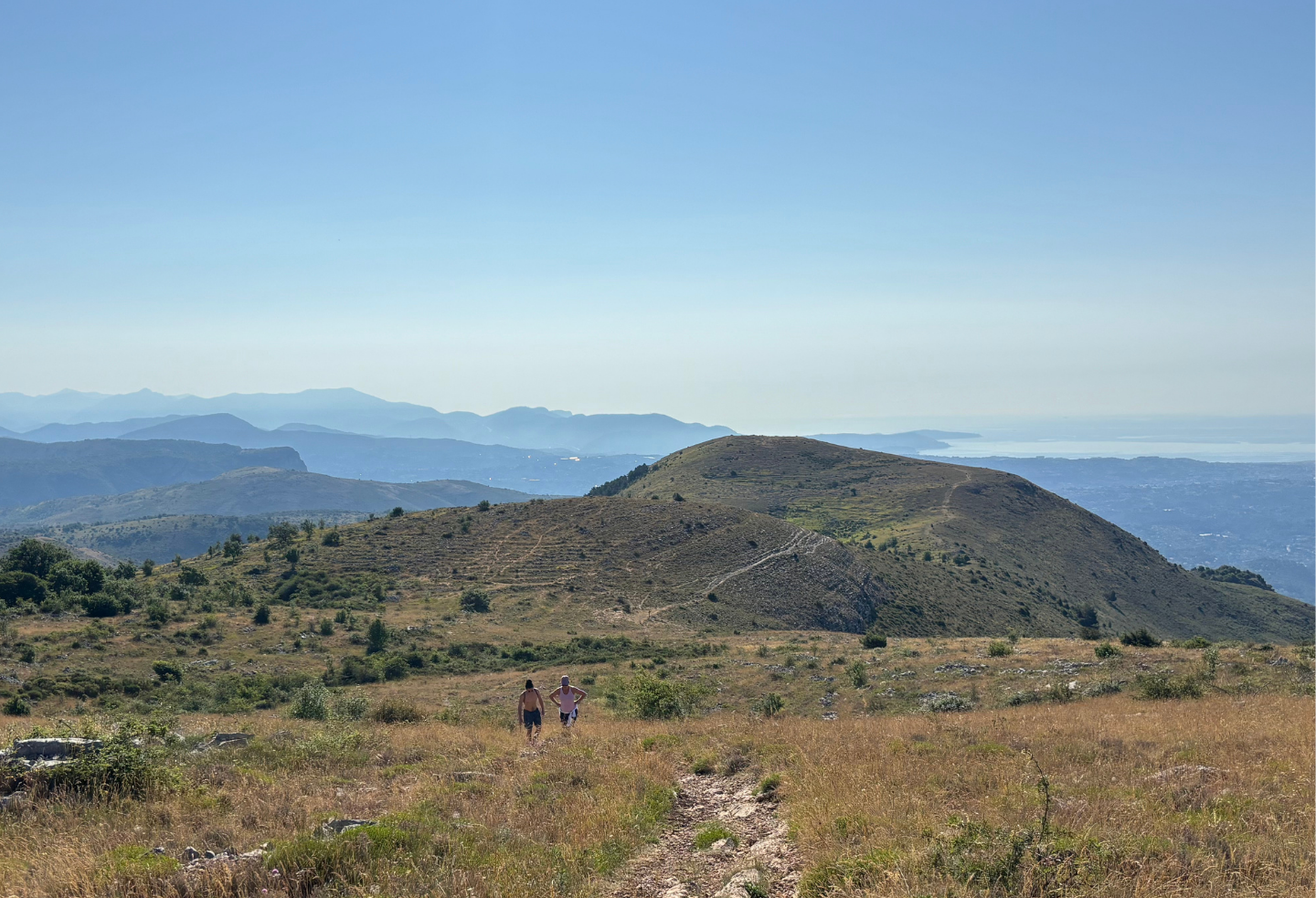 A couple of people standing on top of a grassy hill.