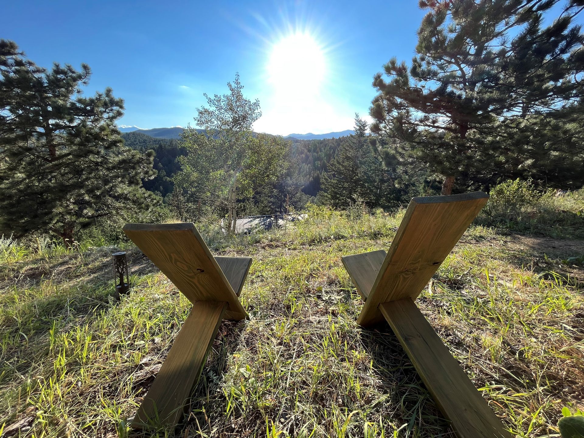 Two wooden chairs face a bright sun over a treed valley.