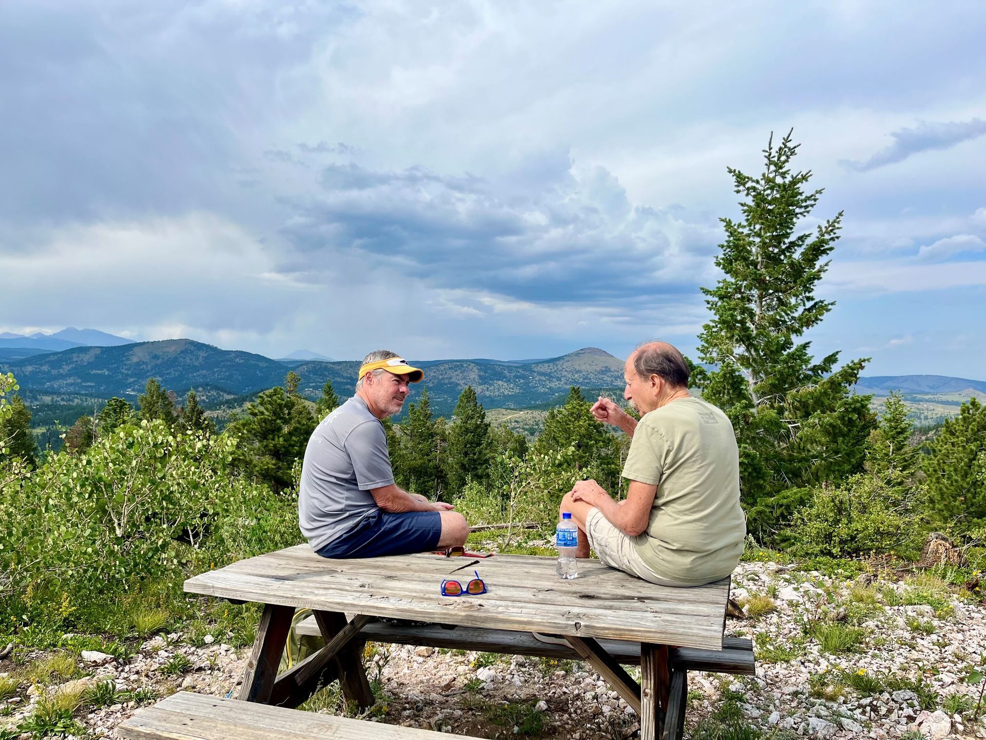 Two people seated at a picnic table, playing a game, with a scenic mountain view.