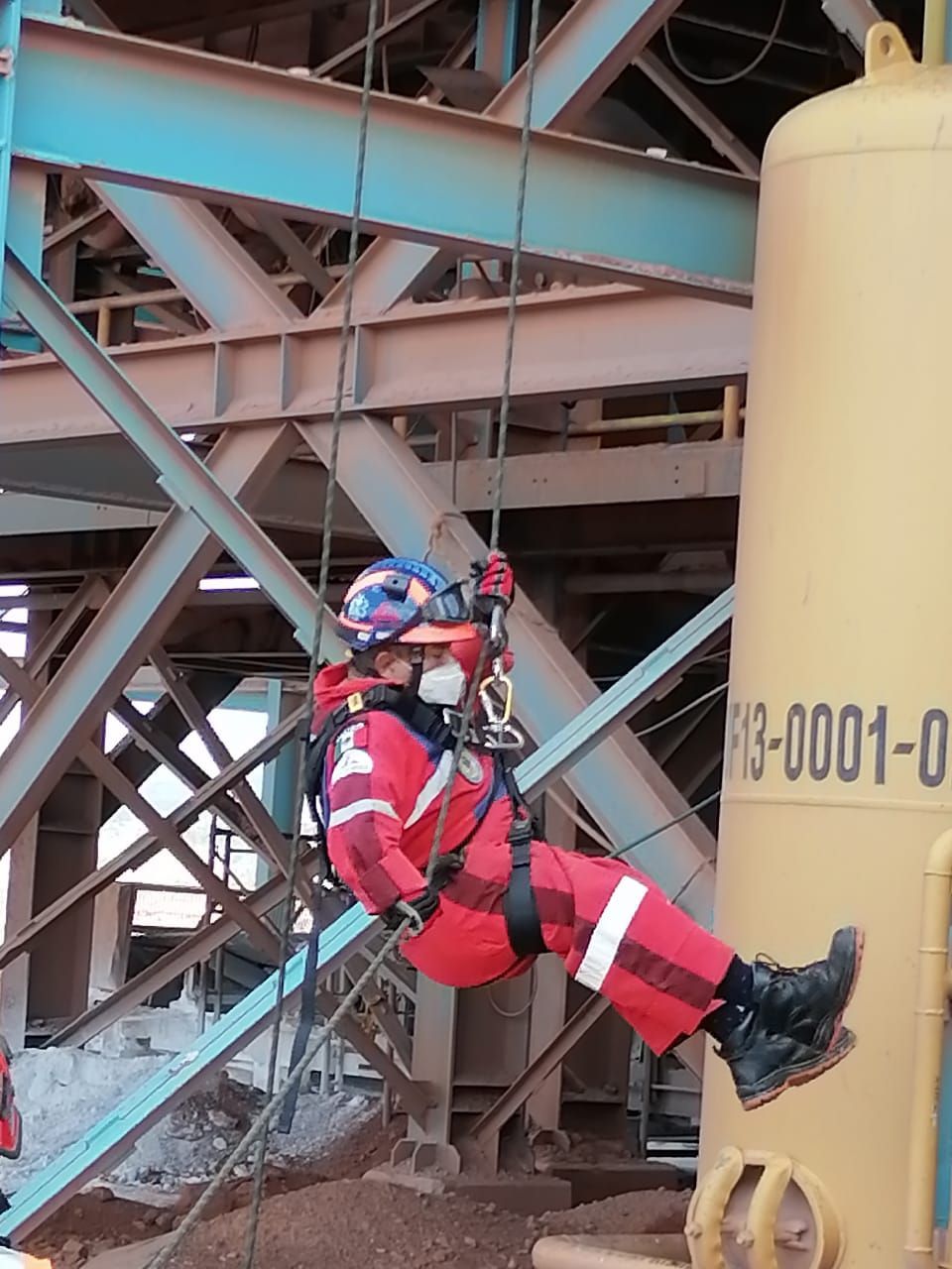 Un hombre está colgado de una cuerda al lado de un tanque amarillo que dice p3-0001-0