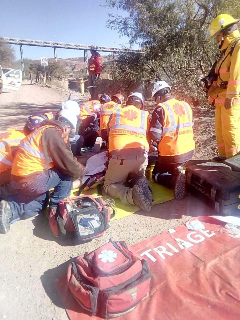 Un grupo de bomberos se arrodilla para ayudar a un hombre en una camilla.