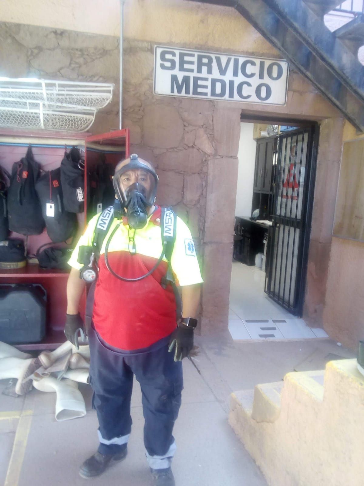 Un hombre que lleva una máscara de gas está parado frente a un cartel que dice servicio médico.