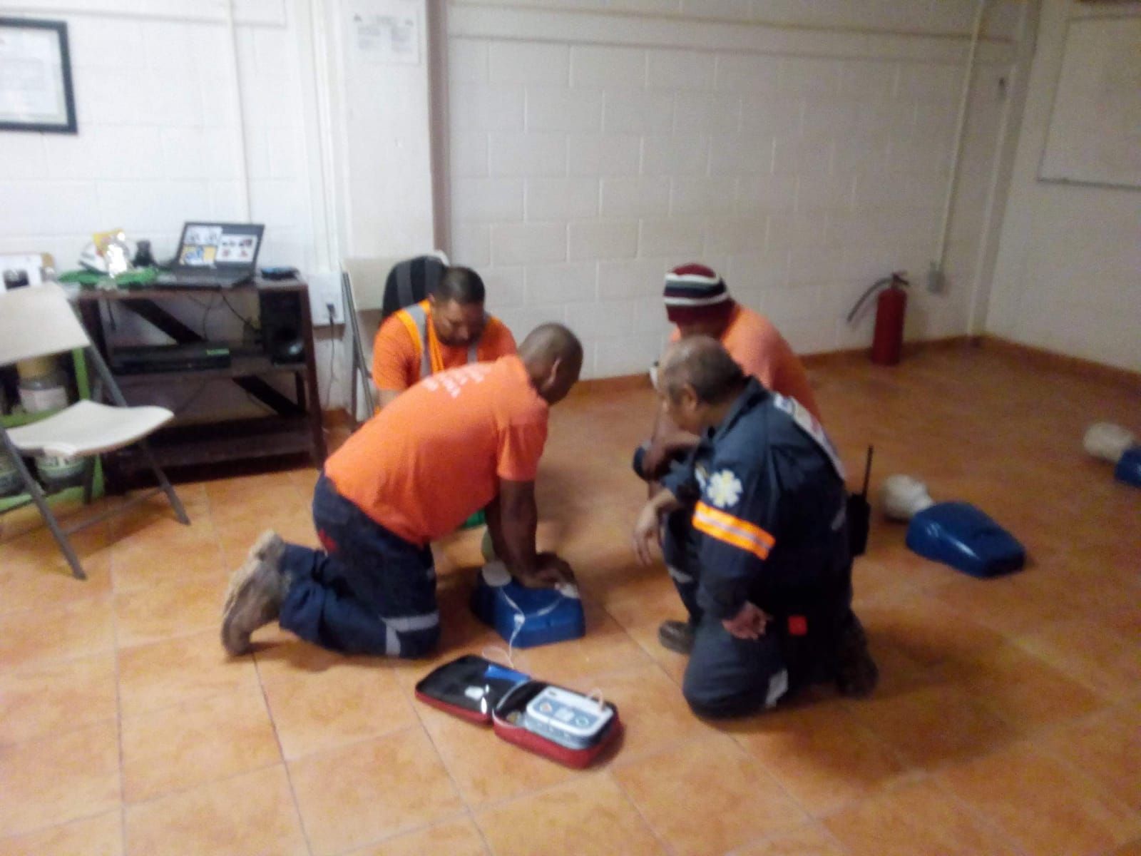 Un grupo de hombres está arrodillado en una habitación con un desfibrilador en el suelo.