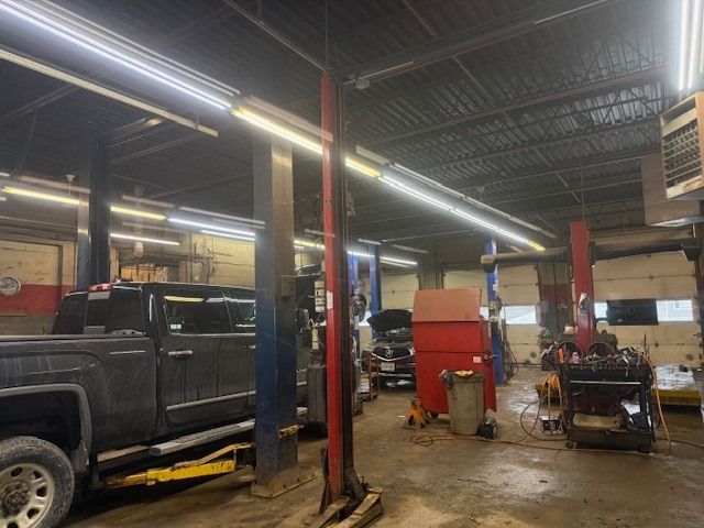An automotive garage workspace featuring a black truck on a lift, red tool cabinets, and overhead industrial lighting. | Orillia Steer And Stop