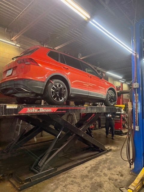 A red Volkswagen SUV sits elevated on a John Bean scissor lift inside an auto repair shop. | Orillia Steer And Stop