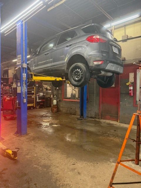 A dark grey Ford EcoSport lifted on a yellow two-post automotive lift inside a garage. | Orillia Steer And Stop