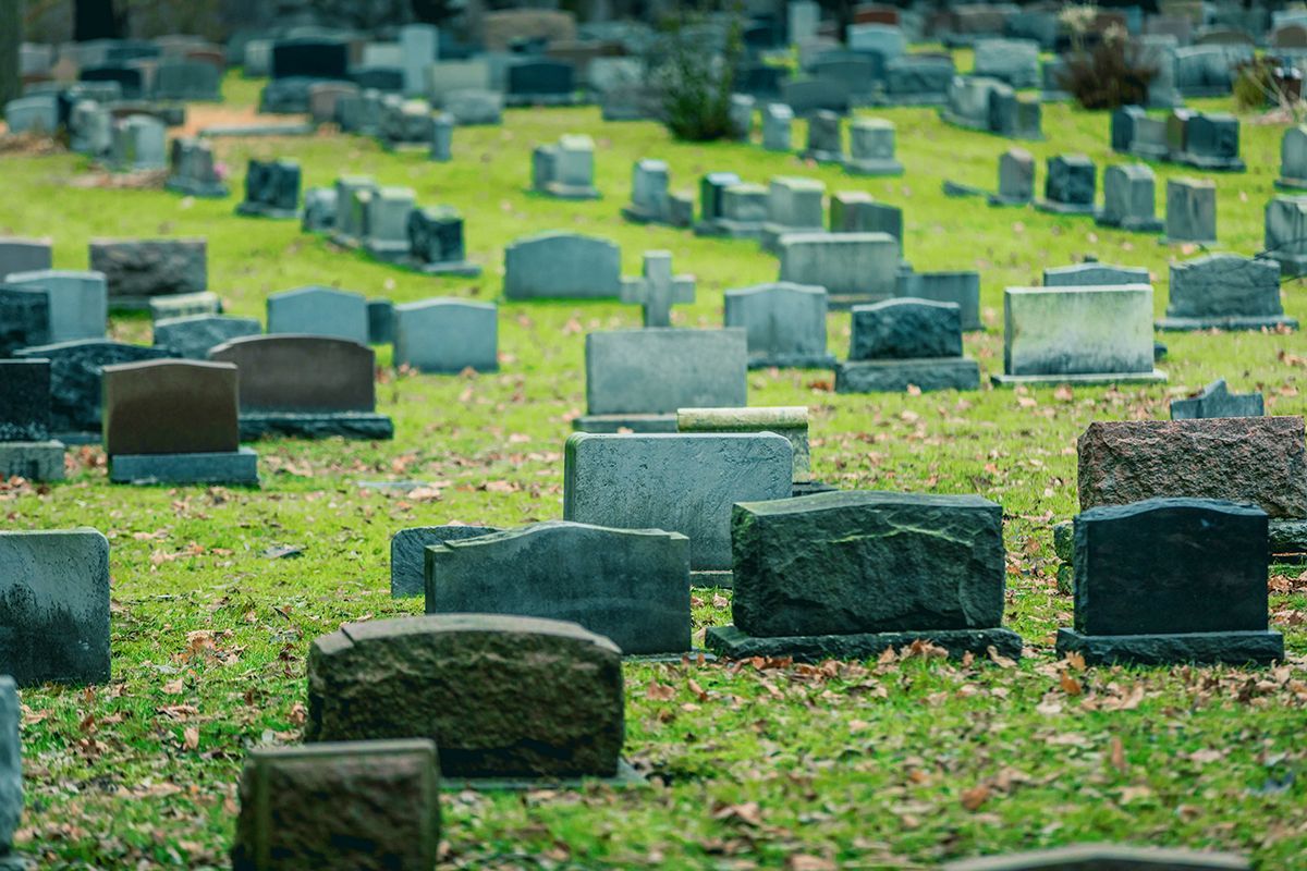 A cemetery filled with tombstones on a grassy hill; many gray stone markers.