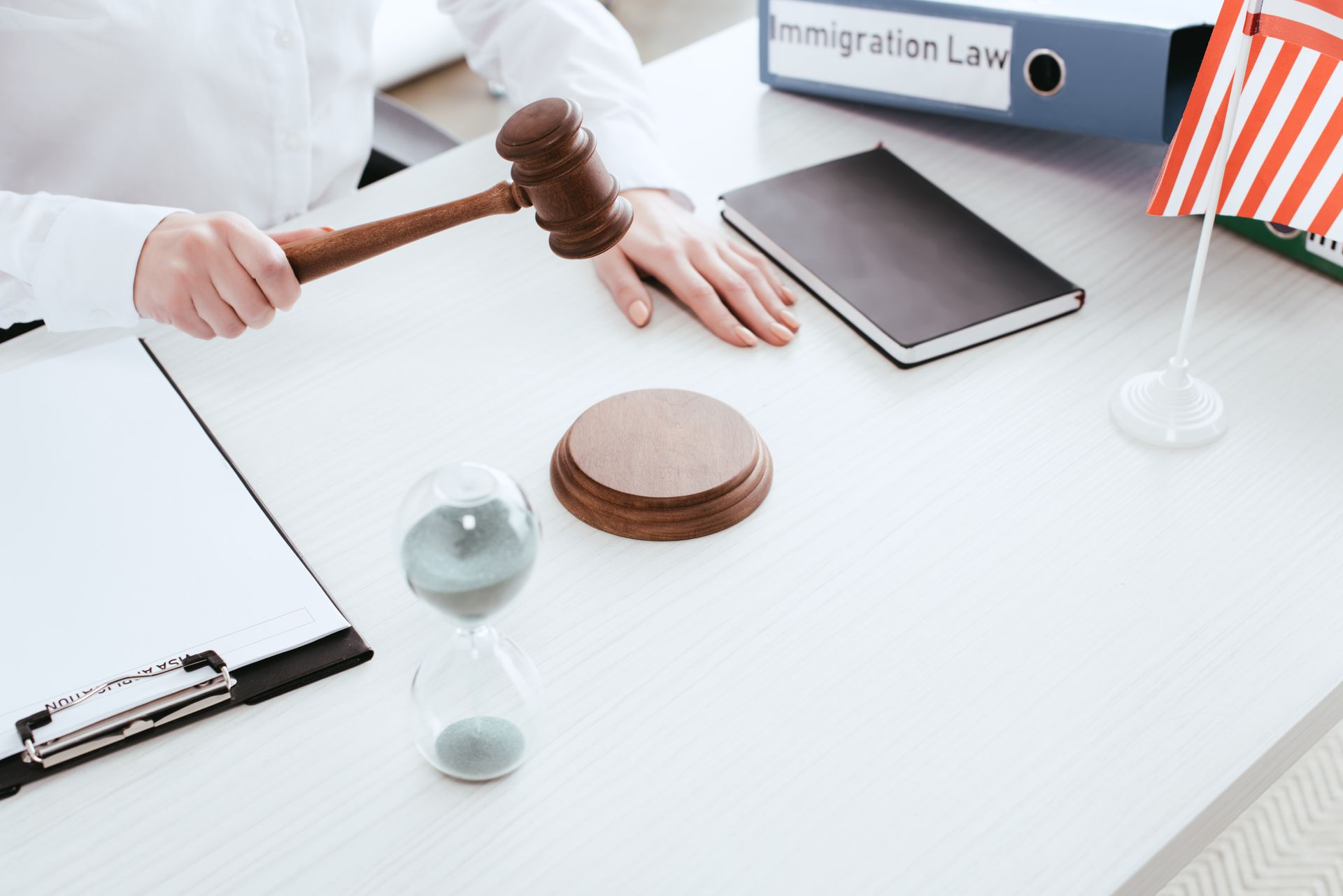 Person holding gavel near a desk with a notebook, hourglass, and US flag, with a file folder labeled