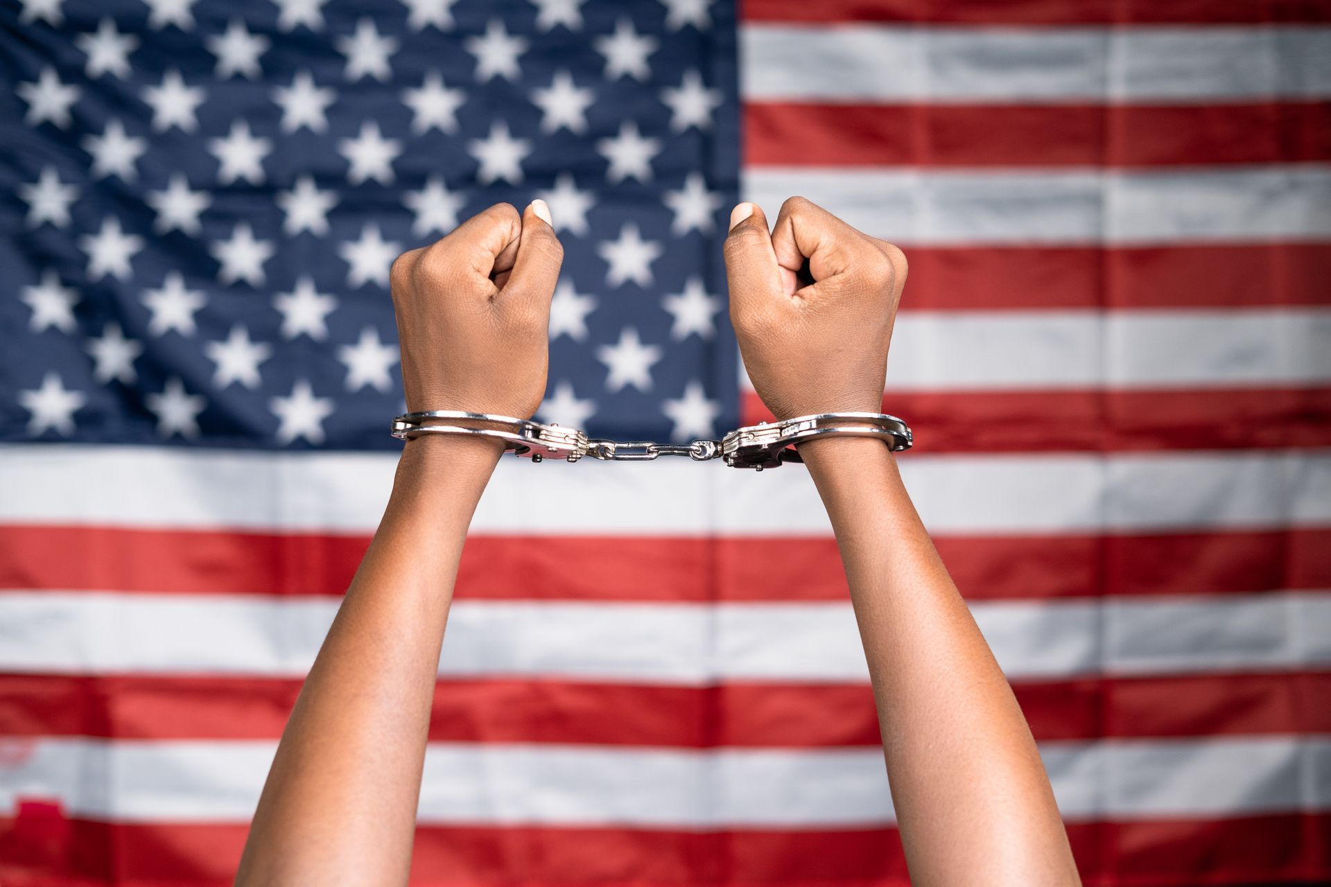 Hands in handcuffs raised against an American flag.
