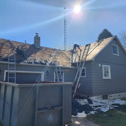 A house with a ladder on the roof and a dumpster in front of it.