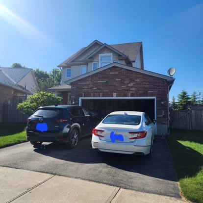 Two cars are parked in front of a brick house.