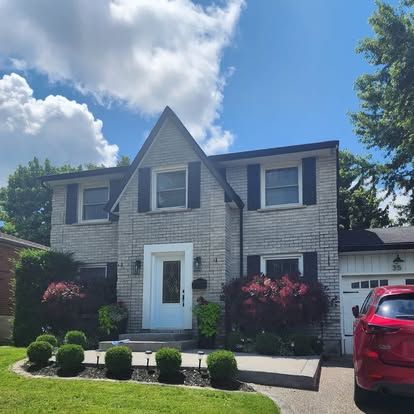 A red car is parked in front of a brick house