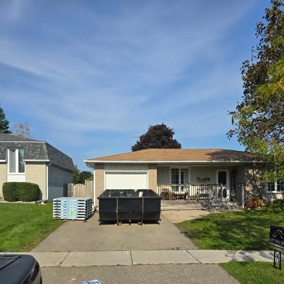 A car is parked in front of a house with a dumpster in the driveway.