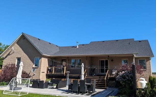 Back of a brick house with a deck, patio, and blue sky. Green lawn and outdoor furniture.