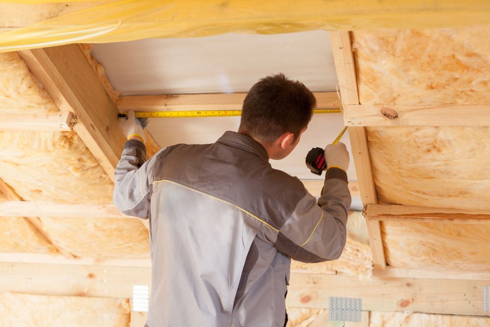 Man measuring wood framing in a structure filled with insulation.