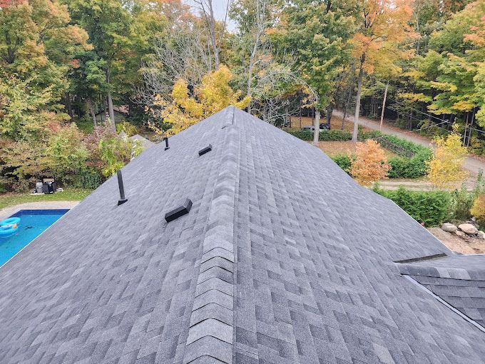 Gray shingled roof with several vents. Fall foliage surrounds a home with a blue pool.