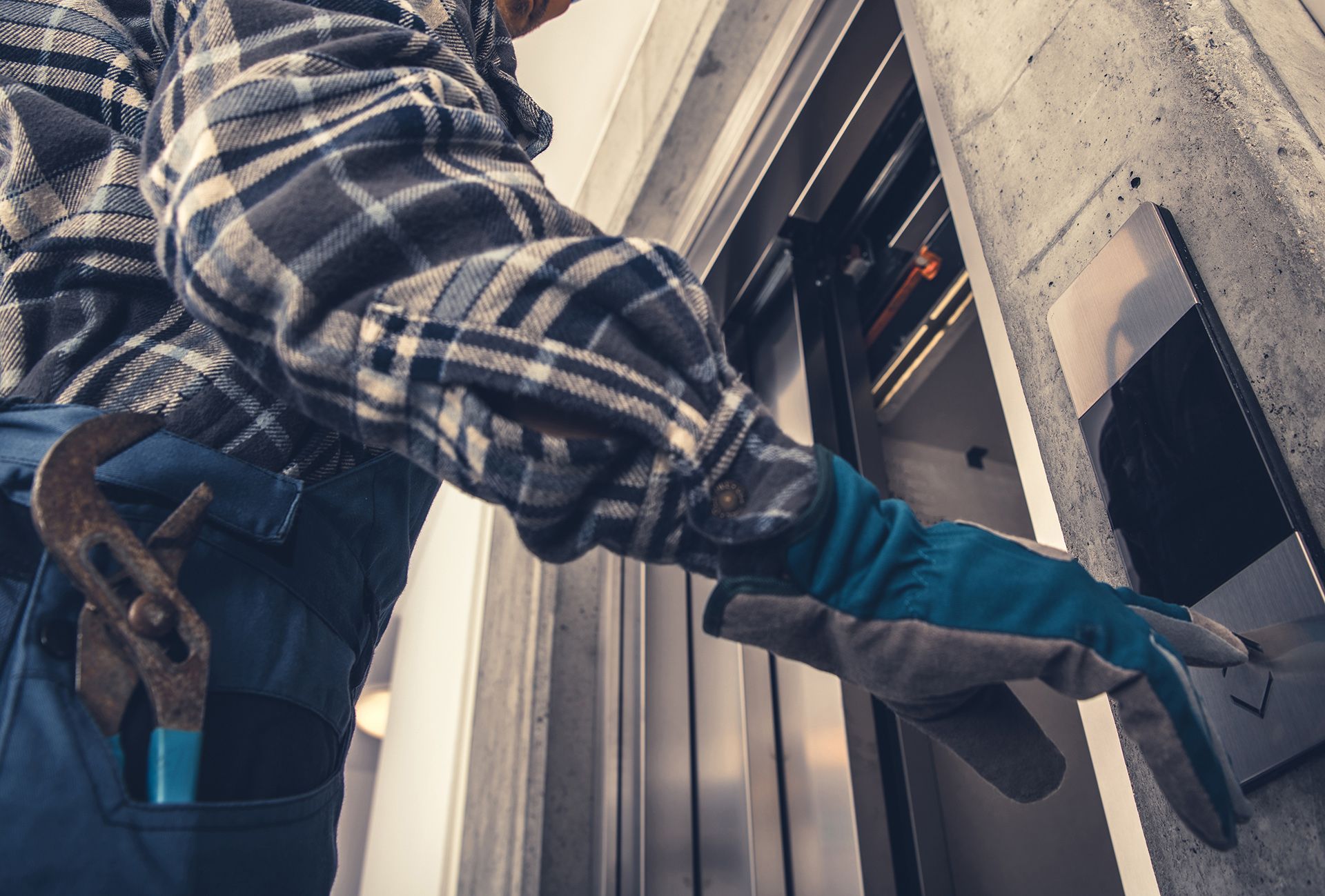 Un hombre está usando una llave inglesa para abrir la puerta de un ascensor.