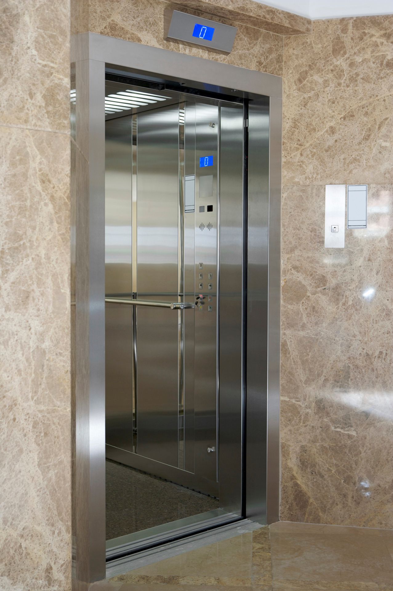 Un ascensor de acero inoxidable con una pared de mármol detrás.