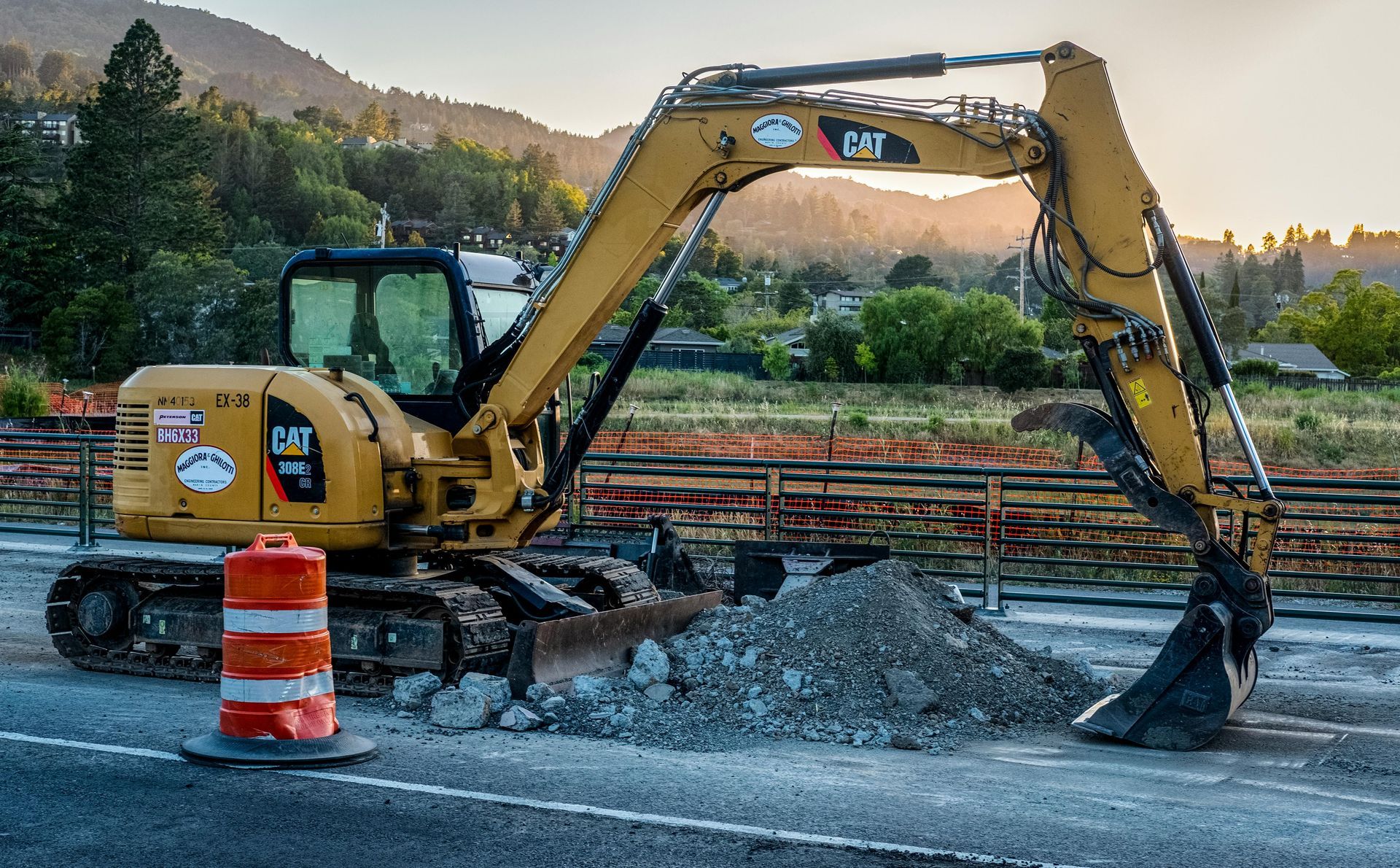 Yellow excavator digging beside a road construction site with orange barrels and rubble.