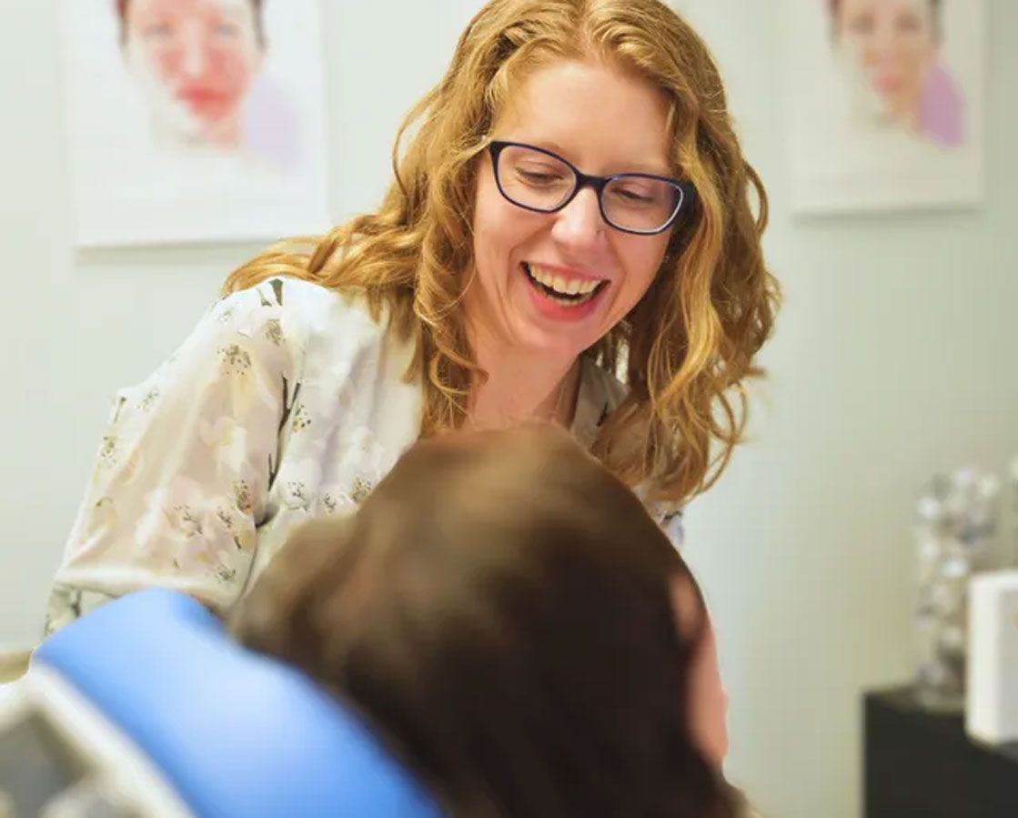 A woman wearing glasses is smiling while talking to a patient.