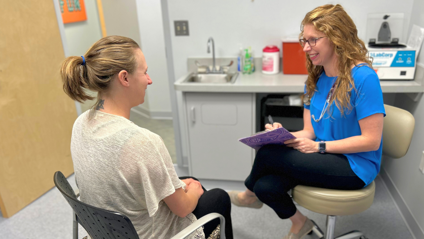 A woman is sitting in a chair talking to another woman.