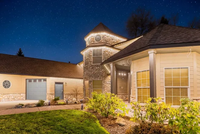 Well-lit suburban house exterior at night with a blue sky and landscaped front yard