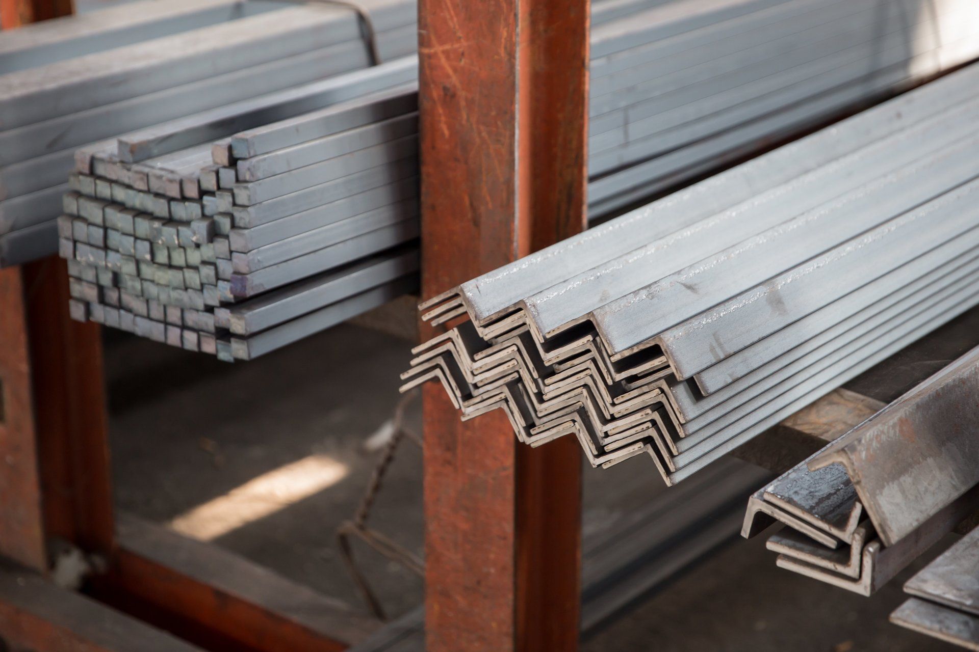 Travi metalliche impilate su scaffali: barre quadrate e angolari di ferro.