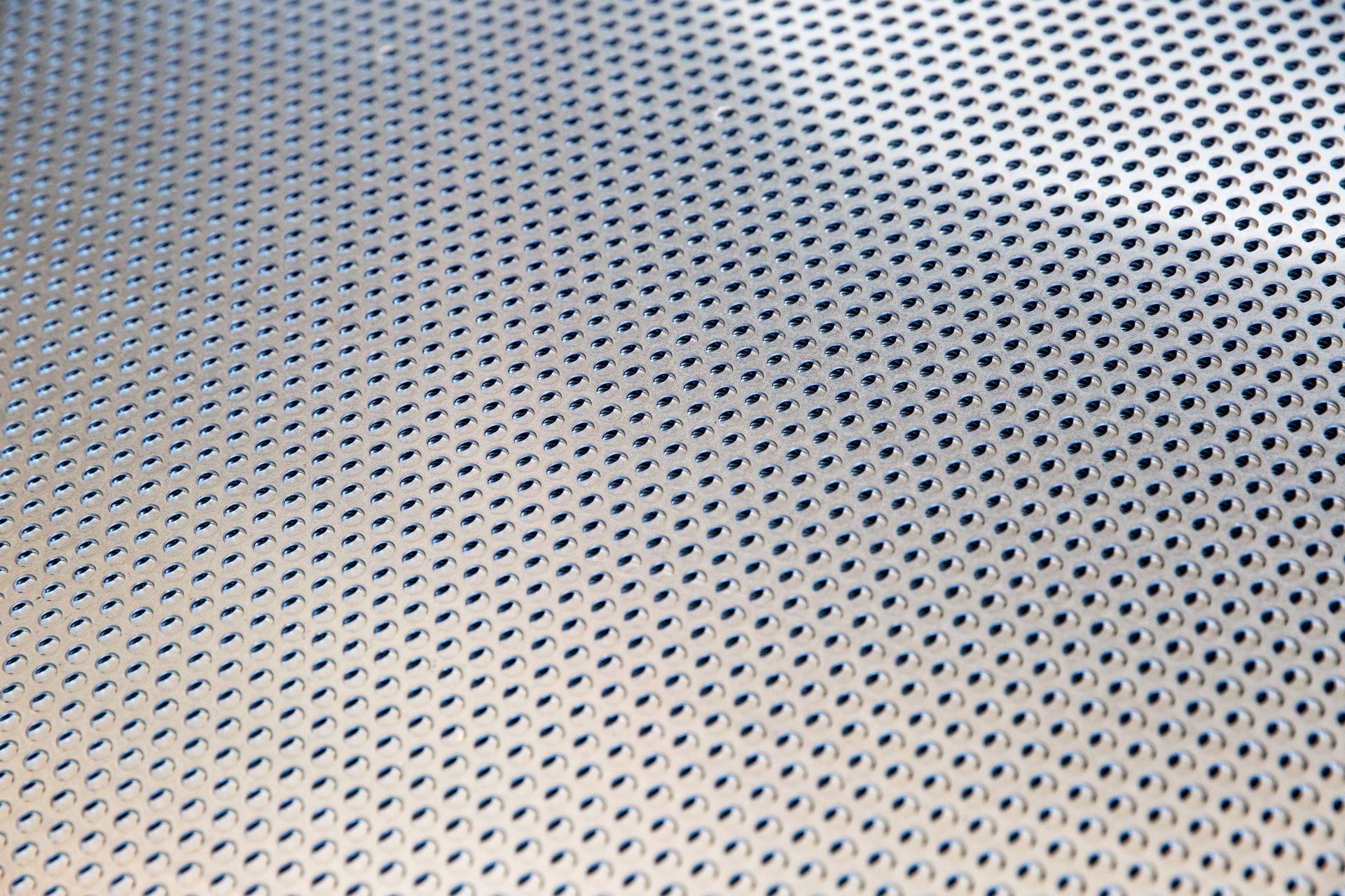 Lamiera metallica perforata con piccoli fori uniformemente distanziati che riflettono la luce.