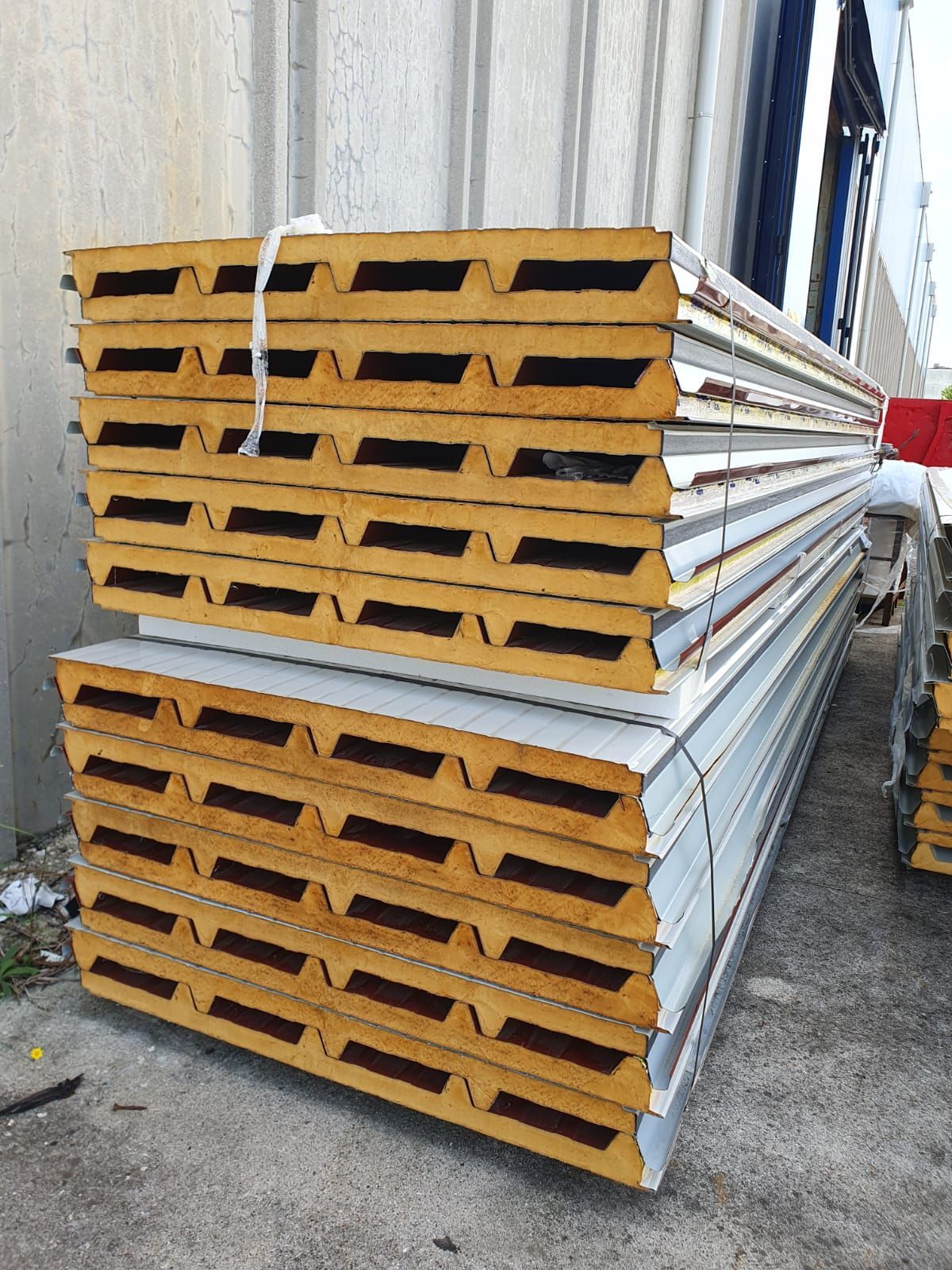 Pannelli sandwich isolati gialli e argentati impilati, probabilmente destinati all'edilizia, all'esterno.