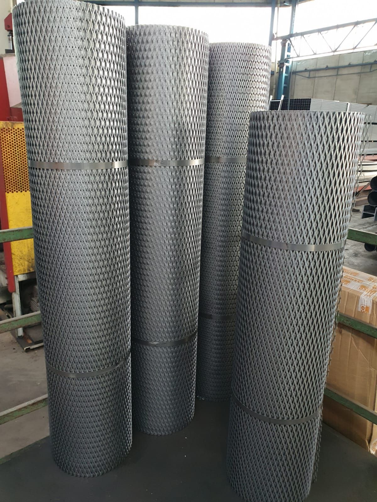 Quattro fogli di lamiera stirata grigia arrotolati e legati insieme all'interno di un magazzino.