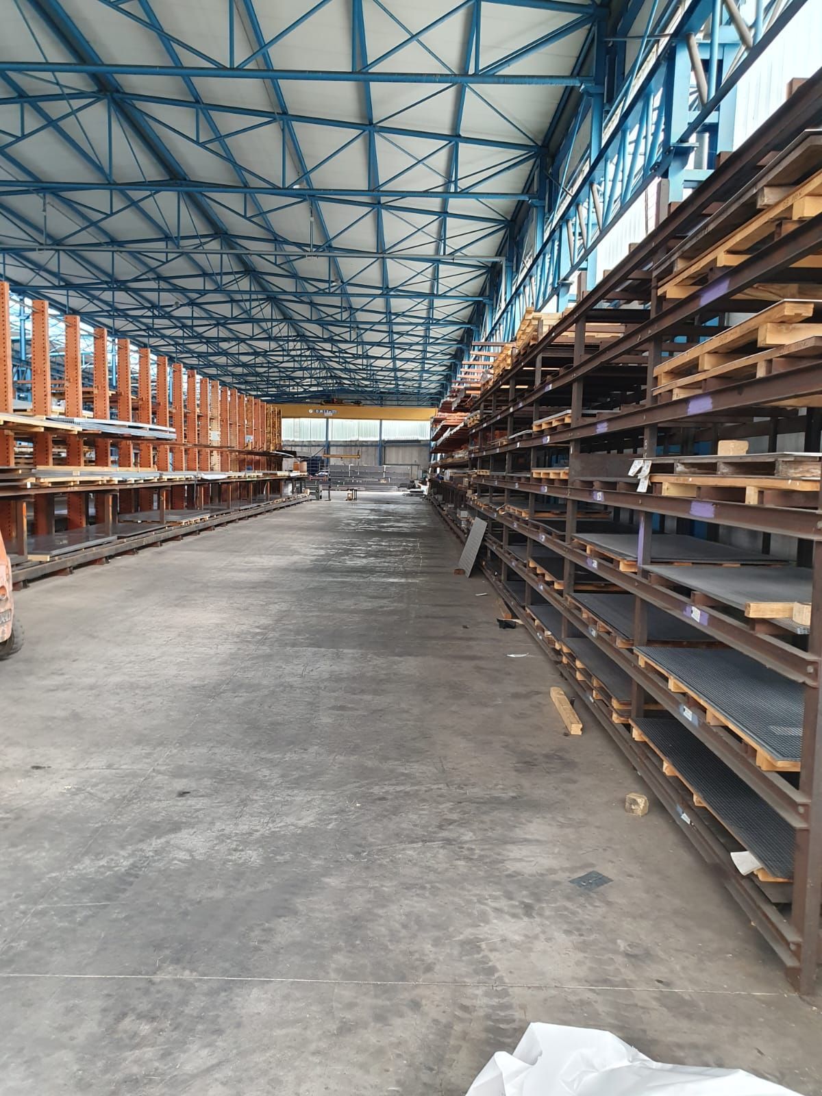 Interno di un magazzino con scaffalature ricoperte di lamiere, lunghe file, soffitto blu.