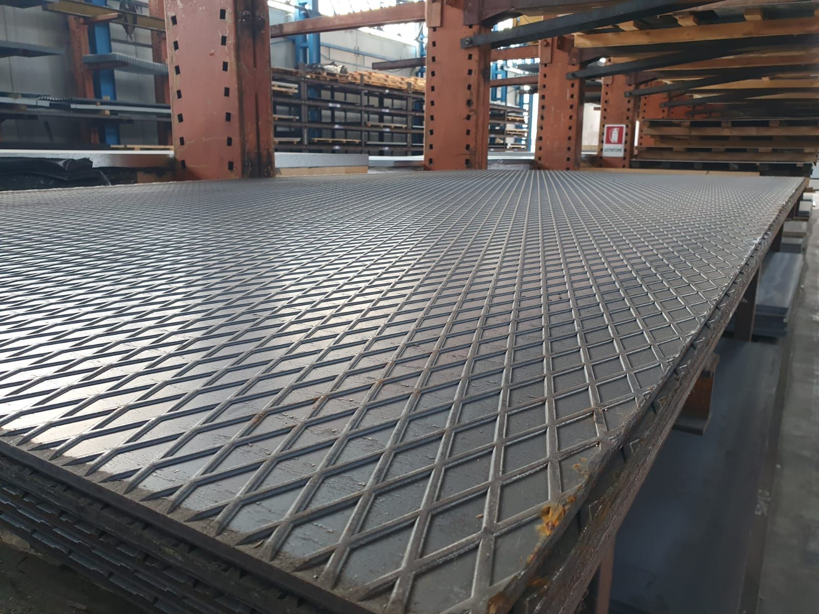 Pila di lamiere diamantate in un magazzino, appoggiate su un pallet.