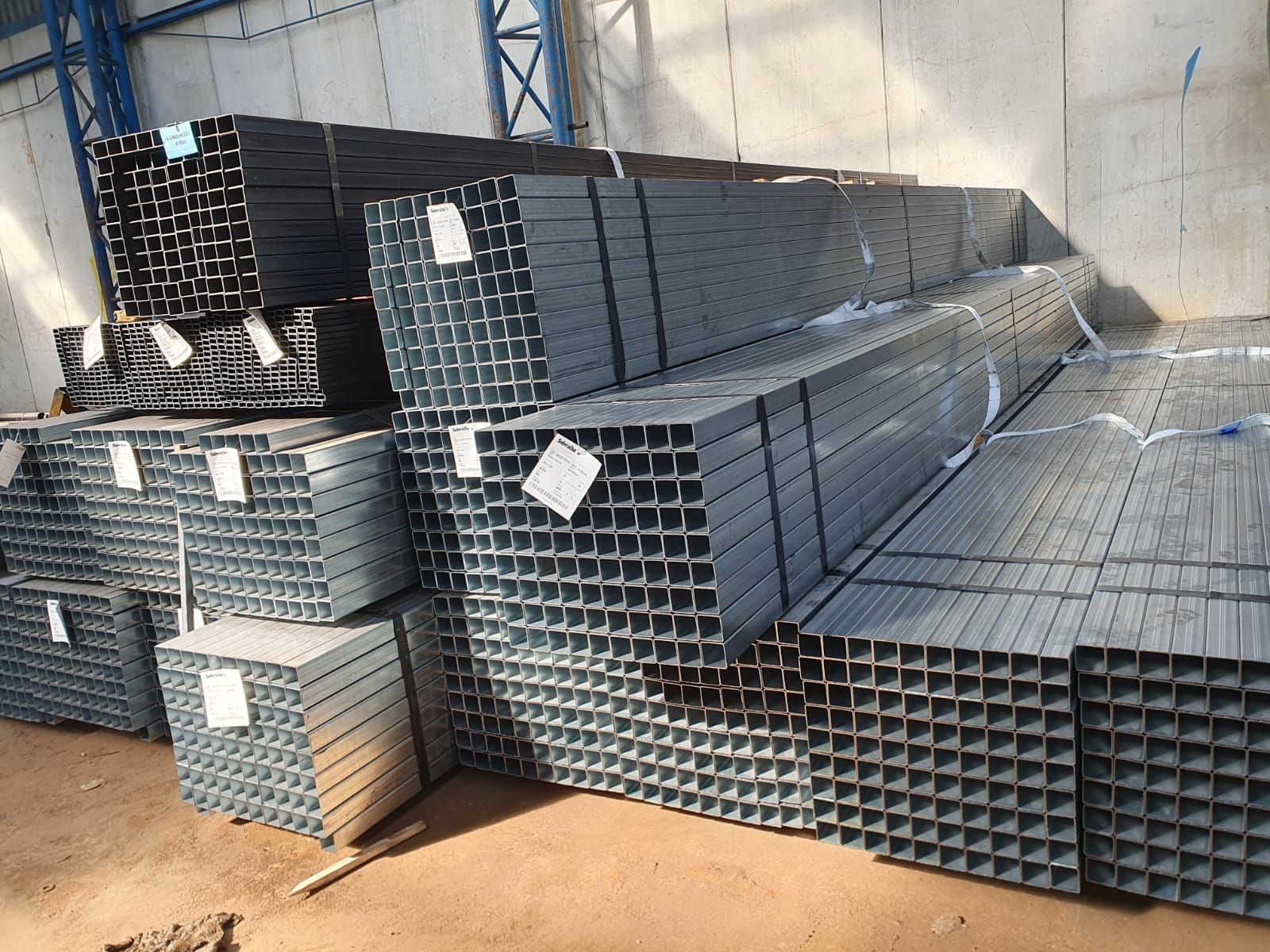 Pile di tubi quadrati di acciaio in un magazzino, metallo grigio, raggruppati ed etichettati.