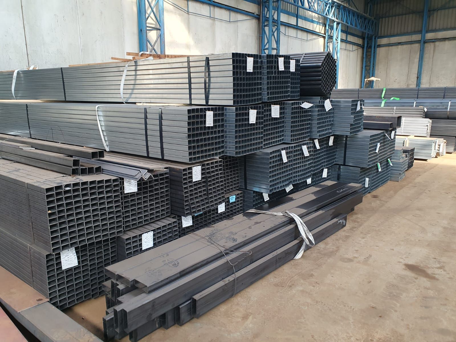 Pile di travi d'acciaio in un magazzino, metallo grigio di varie forme, legate insieme ed etichettate.